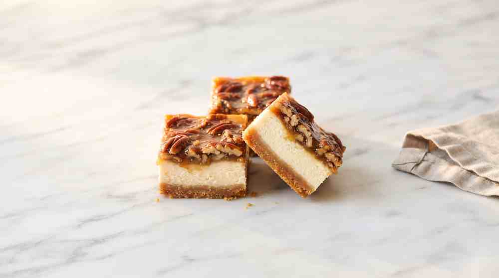 Pecan pie cheesecake bars arranged on marble, one sliced to show the cross-section