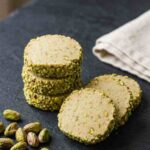 pistachio-shortbread-cookies-hero-shot-1-stacked-cookies-on-dark-slate-with-pistachios